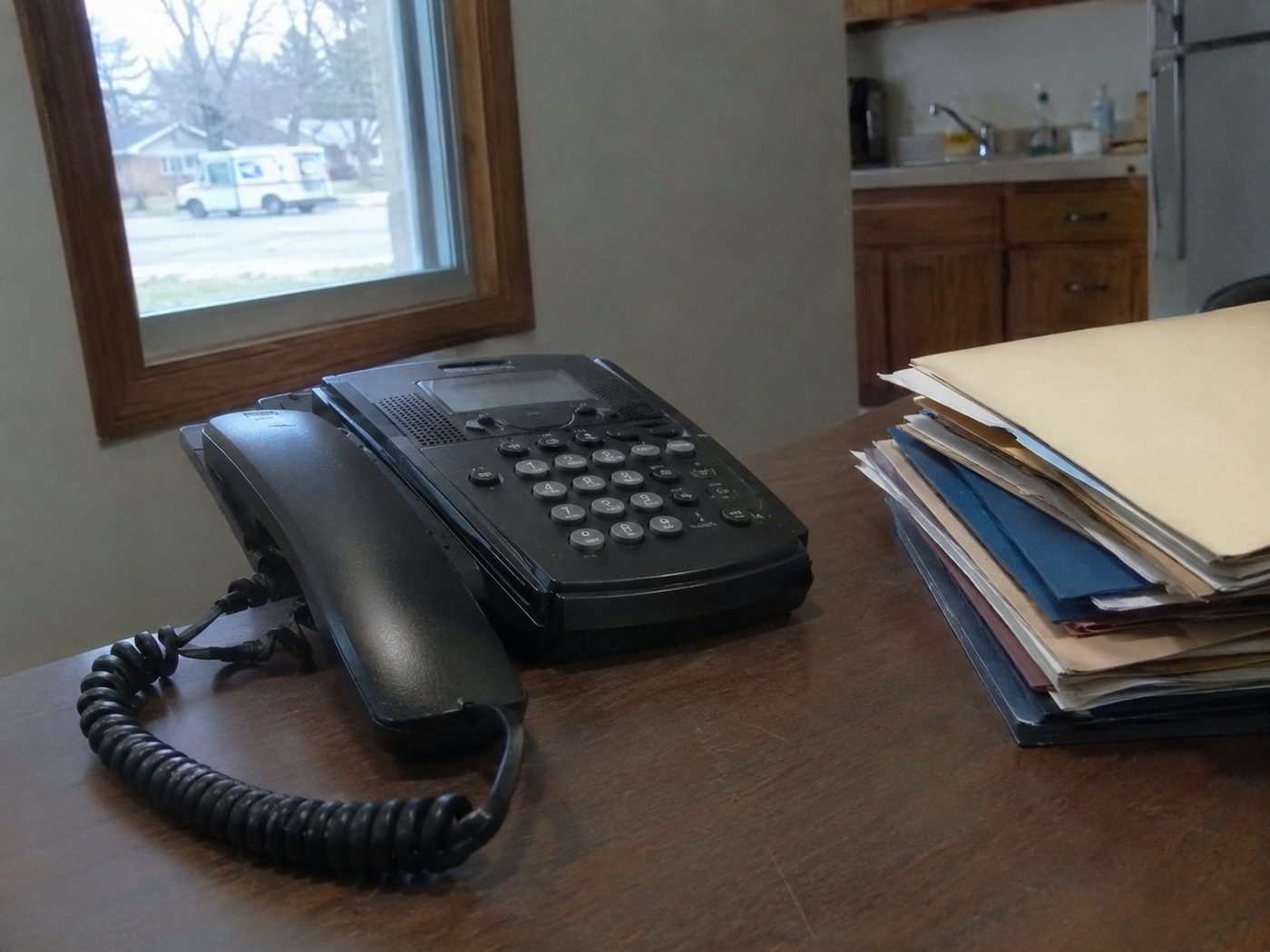 hands setting down a landline phone receiver beside a stack of case folders on a desk