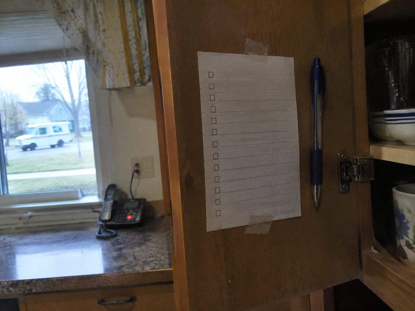 a checklist taped inside a kitchen cabinet door, a pen resting beside it